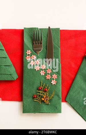 Tovaglioli natalizi in carta con motivi natalizi di colore rosso e verde, vari piegati con posate su superficie bianca Foto Stock