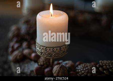 Primo piano di una candela in fiamme in un candelabro con ornamenti su una corona dell'Avvento con coni e noci Foto Stock