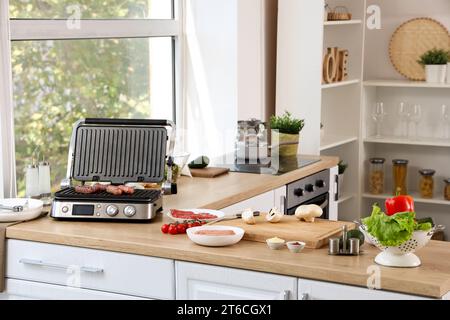 Moderna griglia elettrica con saporite salsicce su ripiano in legno in cucina Foto Stock