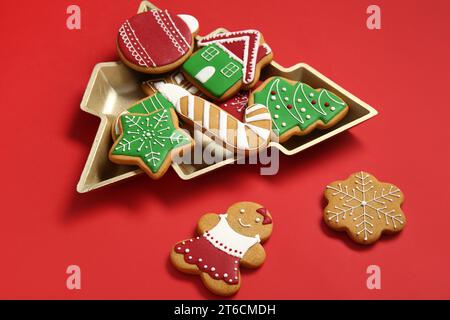 Deliziosi biscotti in un recipiente a forma di albero di Natale su sfondo rosso Foto Stock