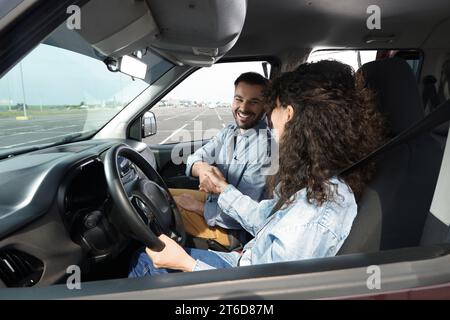 Scuola guida. Allievo felice che stringe la mano con l'istruttore durante la lezione in auto nel parcheggio Foto Stock