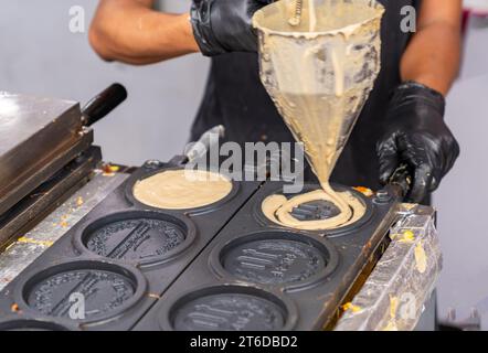 Lo chef lascia cadere la farina fermentata su una padella calda per fare una moneta a forma di pancake, un impasto gommoso pieno di formaggio modellato sulle monete commestibili da 10 won note come Golden 10-Wo Foto Stock