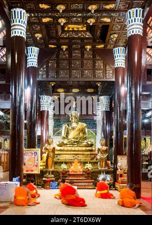 Chiang mai, Thailandia - 20 marzo 2023: Illuminata da luci all'interno dell'antica struttura in legno di teak, i monaci cantano durante le preghiere serali, prima della B dorata Foto Stock