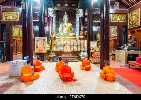 Chiang mai, Thailandia - 20 marzo 2023: Illuminata da luci all'interno dell'antica struttura in legno di teak, i monaci cantano durante le preghiere serali, prima della B dorata Foto Stock