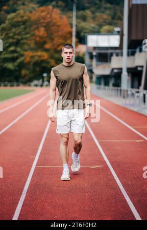 Una figura maschile che corre con sicurezza su una pista da corsa arancione in un ambiente da stadio Foto Stock