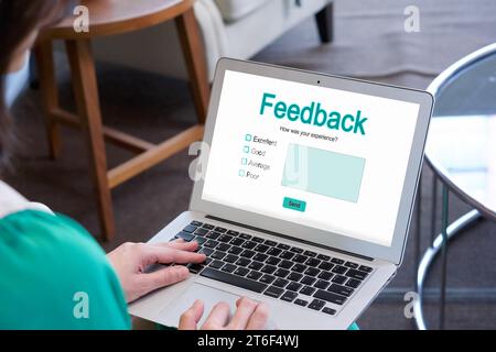 Una signora è impegnata a digitare sul suo computer portatile che mostra un modulo di feedback sullo schermo. Foto Stock