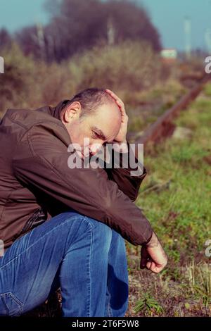 L'uomo premuroso siede su binari. La persona sconvolta in uno stress. Stress concettuale, fallimento della vita, problema. Triste maschio Foto Stock