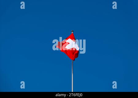 Splendida bandiera svizzera contro Blue Clear Sky in una giornata soleggiata e ventosa in Svizzera Foto Stock