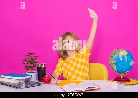 Bambino della scuola che alza la mano, disposto a rispondere alle domande. Il ragazzo della scuola nerd isolato sullo sfondo dello studio. Bambino intelligente della scuola elementare con il libro. Foto Stock