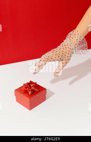 Una donna estende la mano dei guanti a una confezione regalo rossa. Concetto di San Valentino Foto Stock