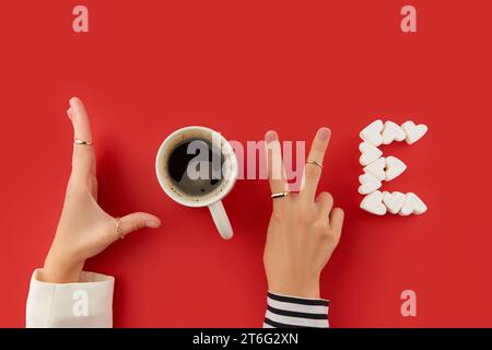 Due mani femminili con unghie in gel rosa che rendono l'amore con una tazza di caffè e marshmallow Foto Stock
