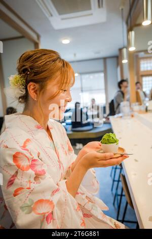 Ritratto di una giovane donna che indossa un kimono estivo yukata giapponese e mangia un gelato matcha in un negozio di tè. Kyoto, Giappone. Foto Stock