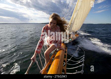 Una ragazza adolescente si arrampica sul boschetto di uno yacht classico mentre naviga lungo la costa del Maine. Foto Stock