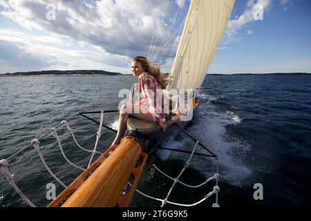 Una ragazzina sorride mentre siede sulla prua di uno yacht classico mentre naviga lungo la costa del Maine. Foto Stock