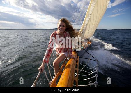 Una ragazza adolescente si arrampica sul boschetto di uno yacht classico mentre naviga lungo la costa del Maine. Foto Stock