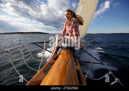 Una ragazza adolescente siede sulla prua di uno yacht classico mentre naviga lungo la costa del Maine. Foto Stock