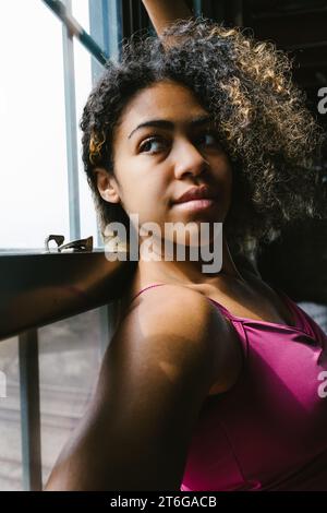 Razza mista giovane adulta femmina con capelli ricci viso e occhi nella finestra Foto Stock