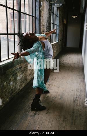 La ballerina posa nel corridoio illuminato dalla finestra in giacca e stivali color ottanio Foto Stock