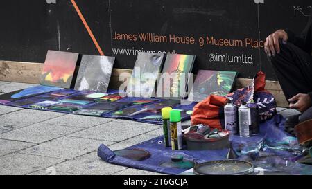 Miseria nel centro di Cardiff. Un senzatetto, con le dita aggrappate nella vernice spray, crea opere d'arte e decora skate board per fare soldi Foto Stock