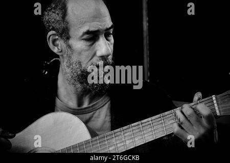 Un artista di strada, le dita si aggrappano alla pittura, suona la chitarra che ha comprato da un altro senzatetto per 5 sterline. Lo usa per busk e integra il suo reddito Foto Stock