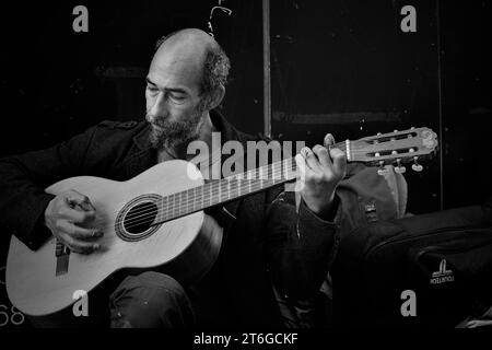 Un artista di strada, le dita si aggrappano alla pittura, suona la chitarra che ha comprato da un altro senzatetto per 5 sterline. Lo usa per busk e integra il suo reddito Foto Stock