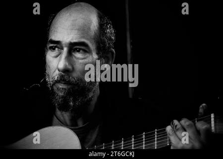 Un artista di strada, le dita si aggrappano alla pittura, suona la chitarra che ha comprato da un altro senzatetto per 5 sterline. Lo usa per busk e integra il suo reddito Foto Stock