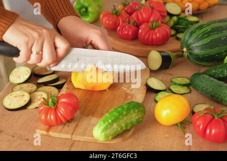 Pomodori grandi maturi, melanzane, verdure su un locale di lavoro in legno della cucina. Molte verdure crude di fondo. Pomodoro, cetrioli. Fornello a casa che fa una h Foto Stock