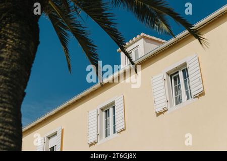 Edificio con persiane bianche e palme a Supetar, Croazia. Cielo blu su sfondo. Concetto minimo. Foto Stock