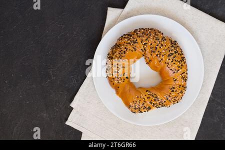 Delizioso simit di bagel turco cosparso di semi di sesamo bianco e nero su un piatto bianco e tovagliolo di lino, sfondo scuro. Vista dall'alto, spazio di copia Foto Stock