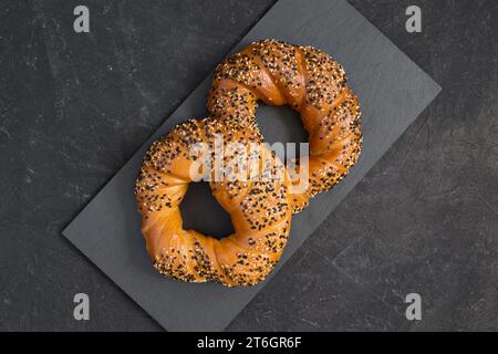 Gustosi bagel tostati freschi cosparsi di semi di sesamo bianchi e neri su sfondo scuro. Bagel turchi o Simits - panificio tradizionale. Vista dall'alto, Foto Stock