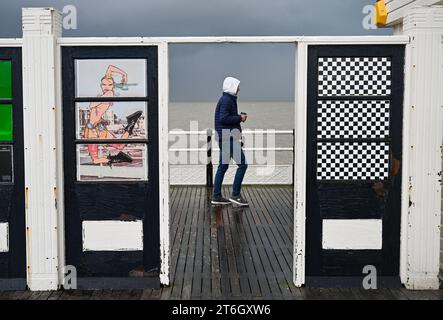 Worthing Regno Unito 10 novembre 2023 - Un visitatore sul molo di Worthing sotto il vento e la pioggia, mentre il maltempo è previsto per il Regno Unito: Credit Simon Dack / Alamy Live News Foto Stock