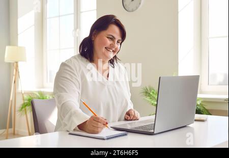 Giovane donna sorridente in sovrappeso che usa un notebook in ufficio Foto Stock