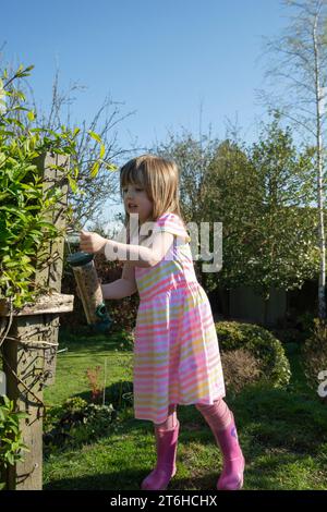 Giovane ragazza che appende un alimentatore di semi d'uccello in un giardino, Co Durham, April Foto Stock