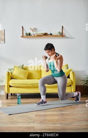 immagine verticale di una giovane donna attraente in abbigliamento sportivo che fa affondi con manubri, fitness e sport Foto Stock