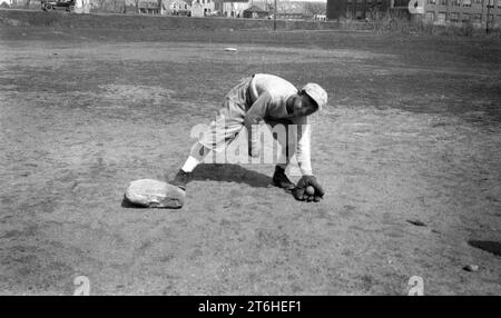 1934, storico, all'esterno dei terreni della Mapplewood Grammar School, un ragazzo che indossa una divisa da baseball e un guanto o un guanto da baseball nella mano sinistra mentre gioca una palla in una base, Stati Uniti Foto Stock