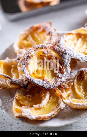 Mini crostate di pasta sfoglia e mele a fette cosparse di zucchero in polvere su piatto bianco. Dolci di mele francesi - primo piano. Foto Stock