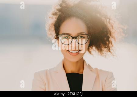 Brillante donna d'affari con capelli ricci e occhiali, che trasmette all'aperto un vestito pastello Foto Stock