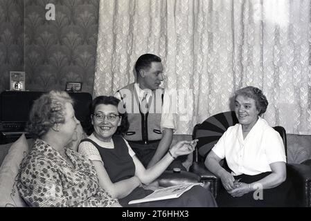 anni '1950, storica, buona compagnia... Tre donne sedute su sedie a sdraio in una camera frontale che parlava e sorrideva, figlio maggiore, che indossava un cardigan senza maniche e zip dell'epoca, seduto accanto a loro ad ascoltare la conversazione, Inghilterra, Regno Unito. Foto Stock