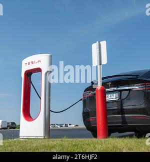 BEMIDJI, MN – 3 giugno 2023: Auto elettrica Tesla nera collegata tramite cavo a una stazione di ricarica Supercharger per la ricarica della batteria. Foto Stock