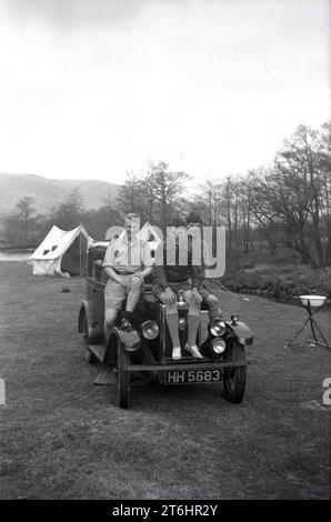 1948, storico, al campo in un campo di campagna con ruscello, tre boy scout seduti per una foto sul cofano di un'auto dell'epoca, Inghilterra, Regno Unito. Foto Stock