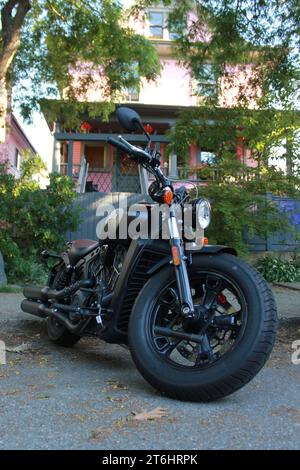 Una motocicletta nera è parcheggiata di fronte a una pittoresca casa rosa a due piani con un cane marrone e bianco in piedi nelle vicinanze Foto Stock