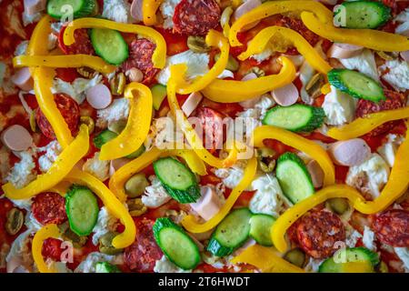 Pizza italiana fatta in casa prima di essere cotta in forno, ripiena di pomodoro, mozzarella, peperoni, zucchine, frankfurters e salame piccante Foto Stock