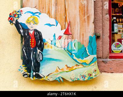 Foto in legno, ragazzo in costume tradizionale nero di fronte alla torre della chiesa, che saluta il bouquet di fiori Kaysersberg, Alsazia Foto Stock