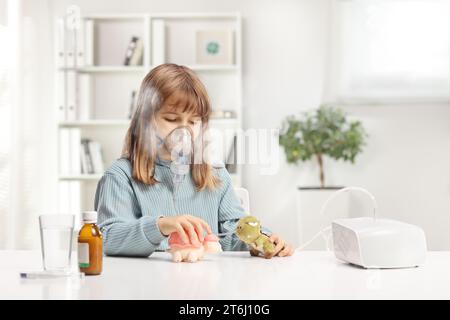 Ragazza che prende un trattamento con nebulizzatore e gioca con i suoi giocattoli Foto Stock