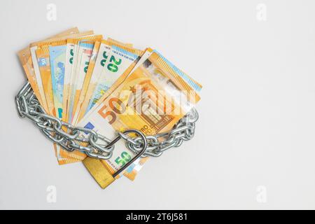 Mucchio di banconote in euro legate con una catena e un lucchetto isolato su sfondo bianco Foto Stock