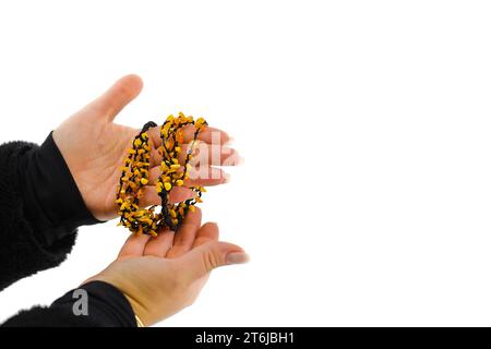 L'immagine presenta una collana ambrata lucida su un cordoncino nero, delicatamente tenuta in mani femminili. Le tonalità dorate contrastano con il nero. Foto Stock