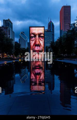 Un volto digitale di uomo con occhi blu brilla sulla Crown Fountain nel Millennium Park, il suo riflesso si specchia nella piscina davanti. Il cartello della società assicurativa Prudential è visibile in alto a destra sull'edificio Prudential. L'artista catalano Jaume Plensa ha creato le torri in mattoni di vetro e schermi LED alte 15,2 metri (50 piedi) nel 2004. Mostrano i volti mutevoli di circa 1.000 residenti di Chicago. Chicago, Illinois, Stati Uniti. Foto Stock
