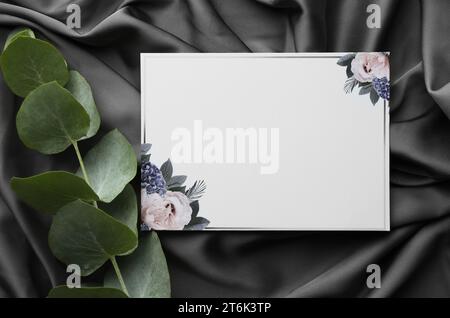 Scheda di invito vuota e foglie di eucalipto su tessuto nero, spianata Foto Stock