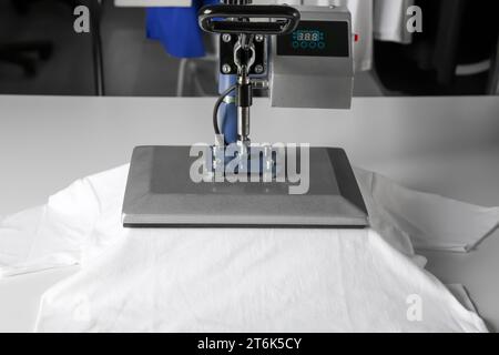 Stampa logo. Pressa a caldo con t-shirt su tavolo bianco Foto Stock