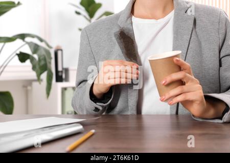 Donna che mostra macchie di caffè sulla giacca al tavolo di legno all'interno, primo piano Foto Stock